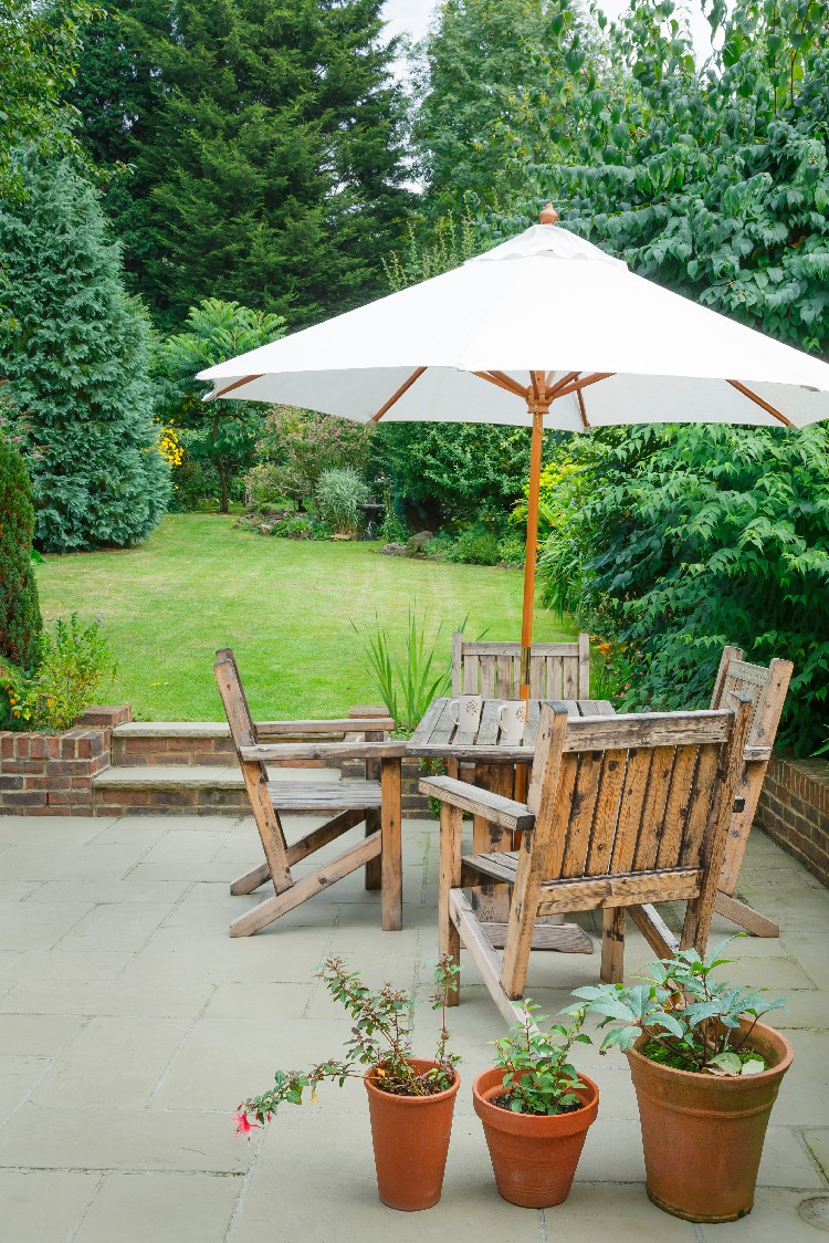 Suburban UK back garden in summer with patio, wooden garden furniture and a parasol or sun umbrella